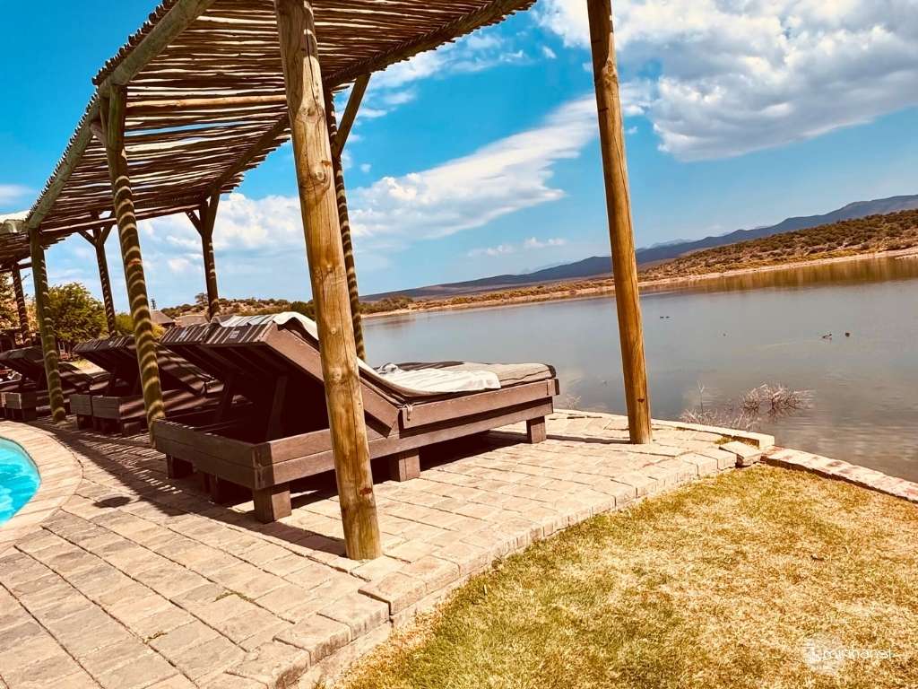 Südafrika - in der Buffelsdrift Game Lodge in Oudtshoorn - Hochwertige Liegen am Pool mit Blick auf den See Südafrika - in der Buffelsdrift Game Lodge in Oudtshoorn - Hochwertige Liegen am Pool mit Blick auf den See